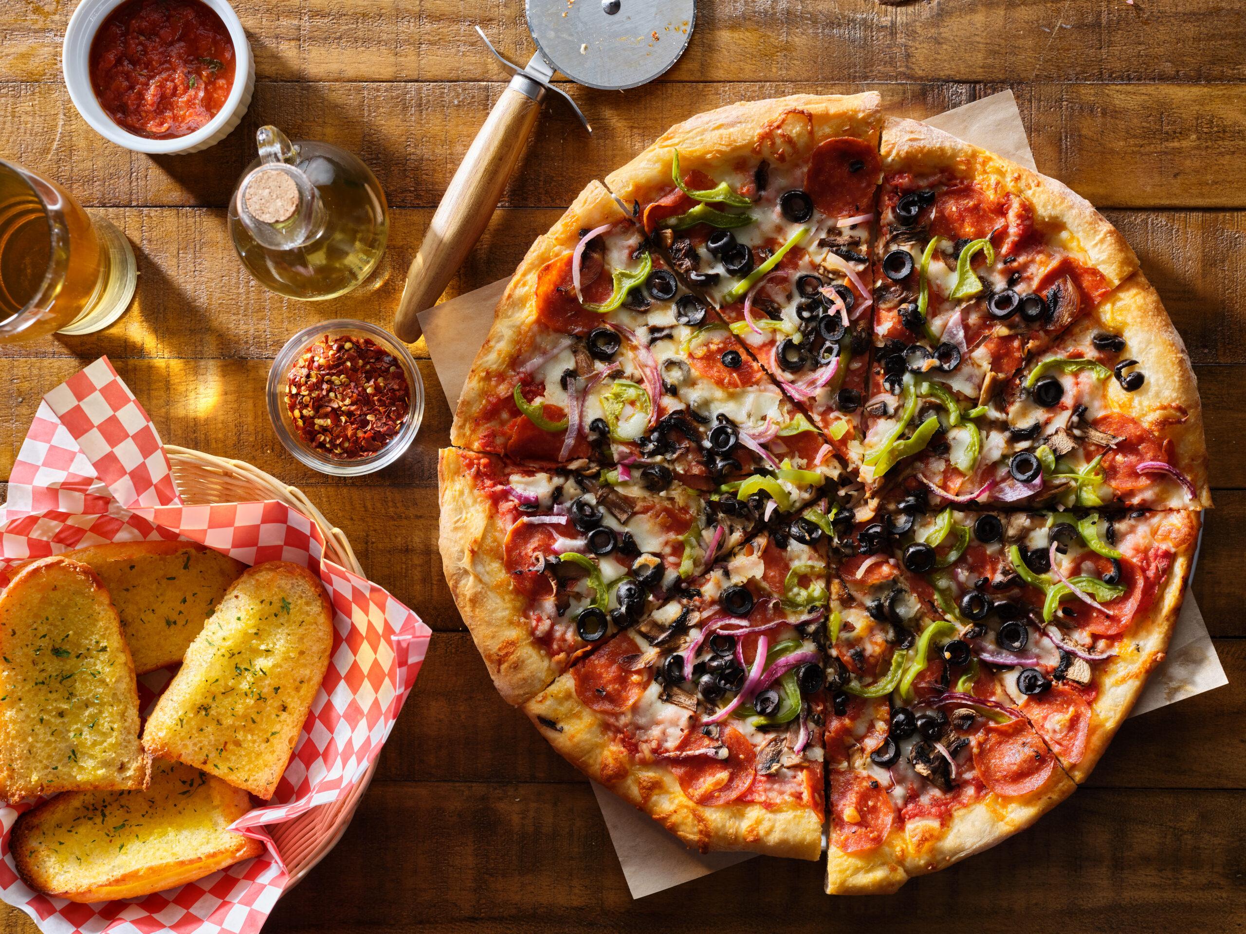 Salami-Pizza mit schwarzen Oliven und Peperoni, sowie Knoblauchbrot.